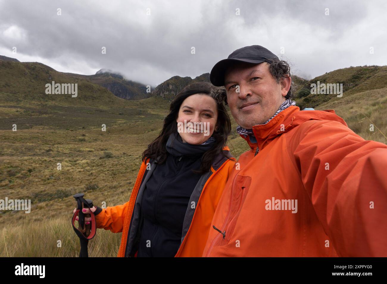 Ein junges Paar in roten Jacken, das an einem bewölkten Tag mitten im Moor ein Selfie mit Bergen im Hintergrund macht Stockfoto