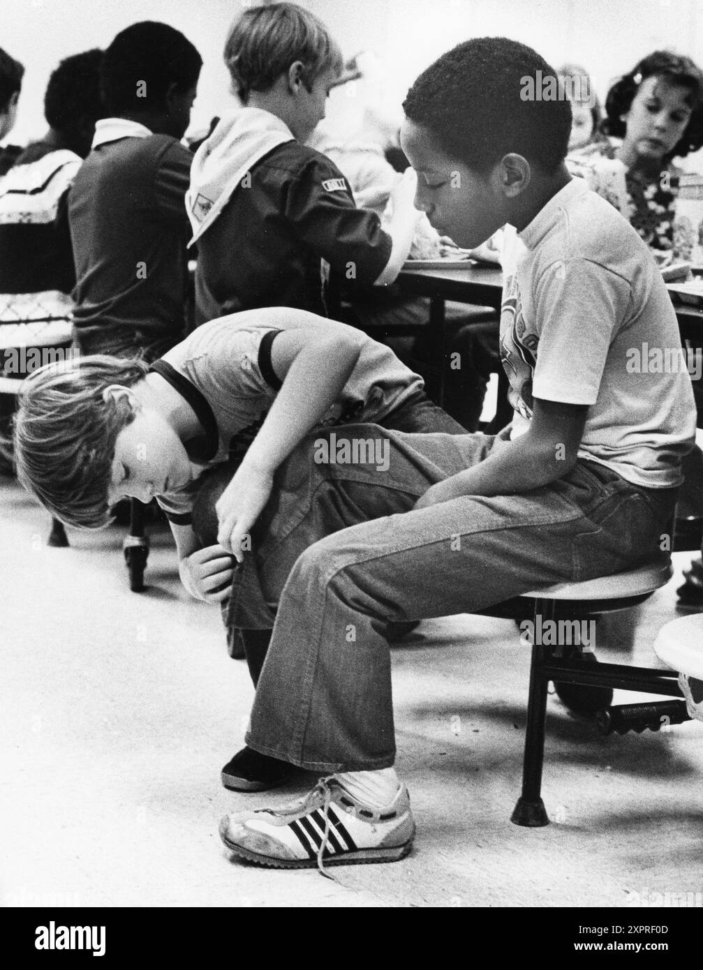 Austin Texas USA, 1984: Patrick Skeaton, der sein rechtes Bein wegen Spina bifida verlor, interagiert mit einem neugierigen Klassenkameraden in der Schulcafeteria der Wooten Elementary. Später wurde er mit einer Beinprothese ausgestattet. Teil einer erweiterten Fotofunktion. ©Bob Daemmrich Stockfoto