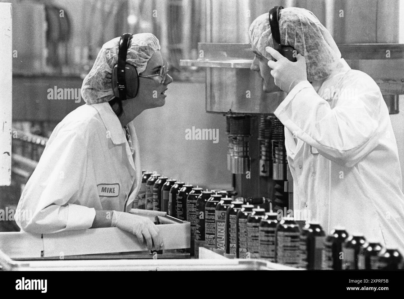 Waco Texas USA, um 1992: Mitarbeiter, die Schutzausrüstung wie Handschuhe, Haarnetze, Laborkittel und Gehörschutz tragen, sprechen über die Produktionslinie im Pharmawerk Allergan. ©Bob Daemmrich EH-0225 Stockfoto