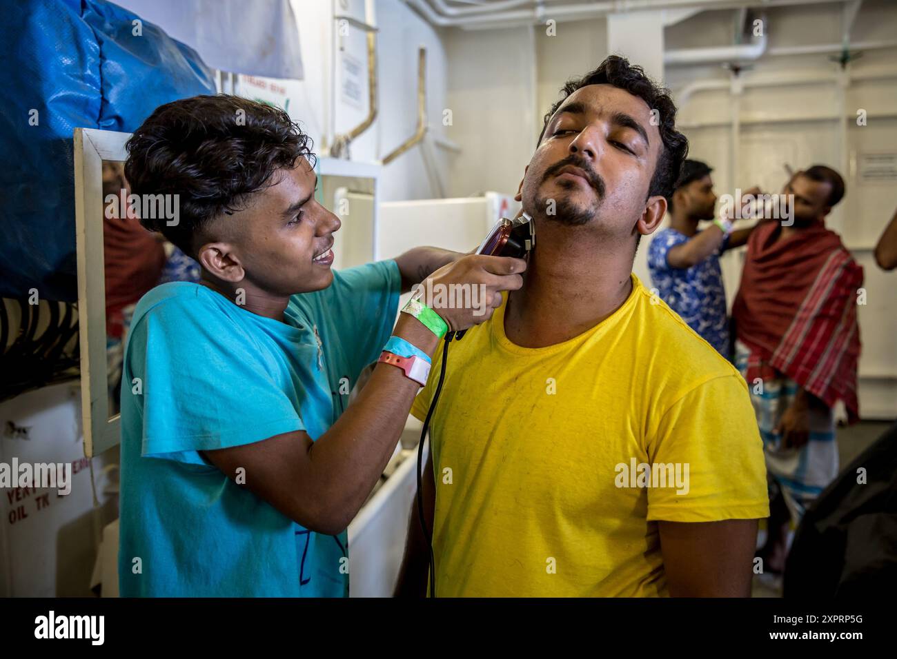 Bangladeshis, die von der Besatzung der Geo Barents gerettet wurden, einem Rettungsschiff, das im zentralen Mittelmeer von Médecins sans Frontières betrieben wird, geben einander Frisuren, nachdem ihnen Ausrüstung zur Verfügung gestellt wurde. Viele sind vor kurzem aus Schmugglern oder Haftanstalten geflohen. UN-Zahlen zeigen, dass seit 2014 mehr als 30.000 Menschen im Mittelmeer gestorben oder vermisst sind, während sie versucht haben, Europa zu erreichen. Stockfoto