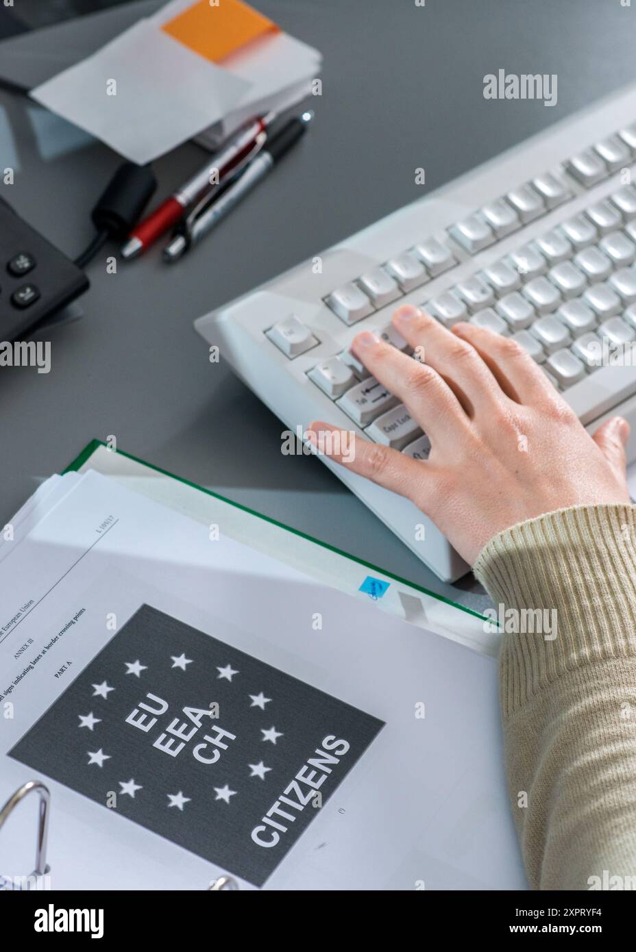 Eine Person, die auf einer Computertastatur im FRONTEX-Lagezentrum in Warschau tippt, mit einem Dokumentenordner für EU-Bürger auf dem Schreibtisch. Das Bild repräsentiert Überwachung, Grenzkontrolle und Koordinierung durch die Europäische Union. Stockfoto