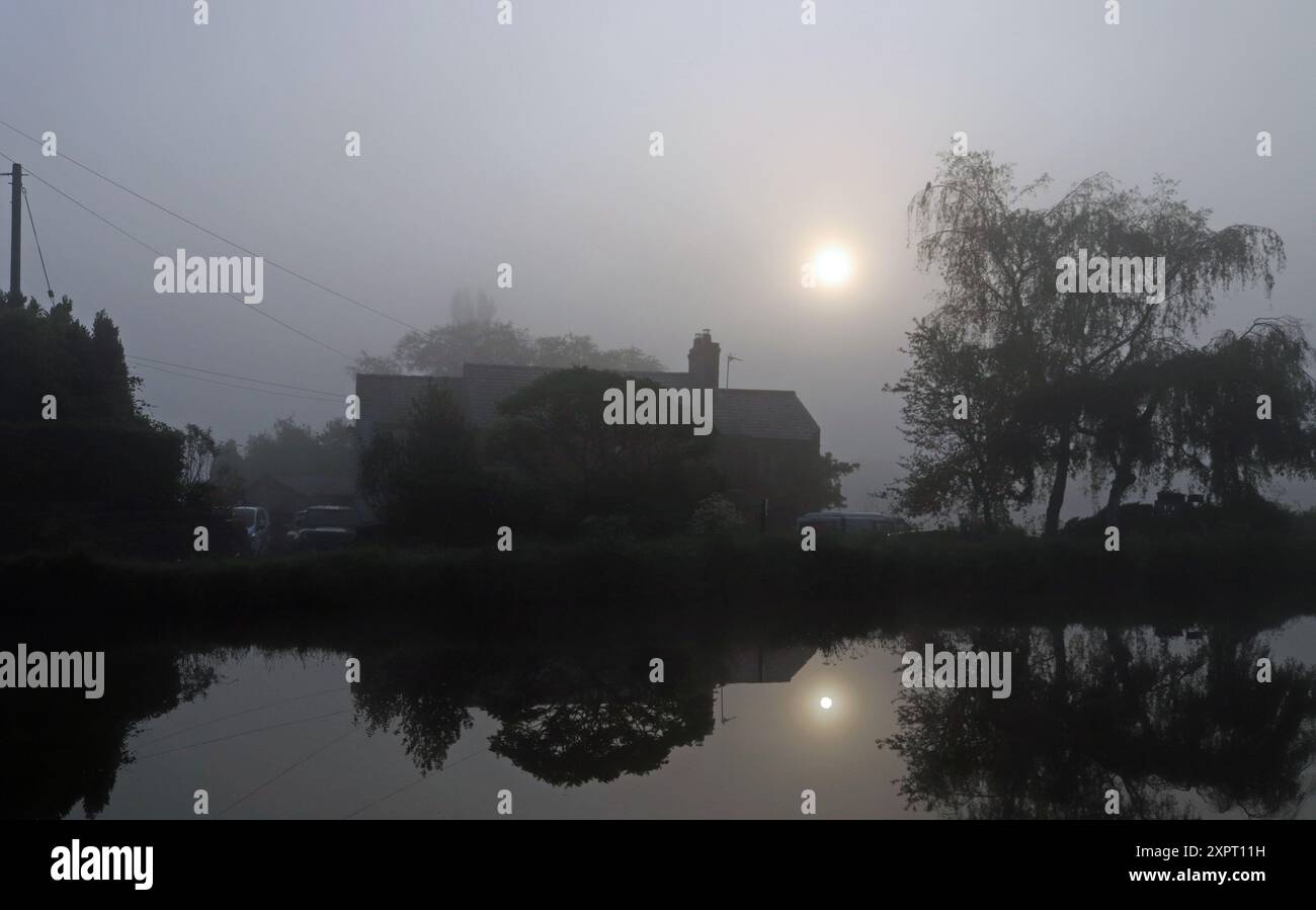 Nach einer kühlen Mainacht fällt es der Sonne schwer, den Morgennebel über den Hütten entlang des L und L Kanals bei Burscough abzutreiben. Stockfoto