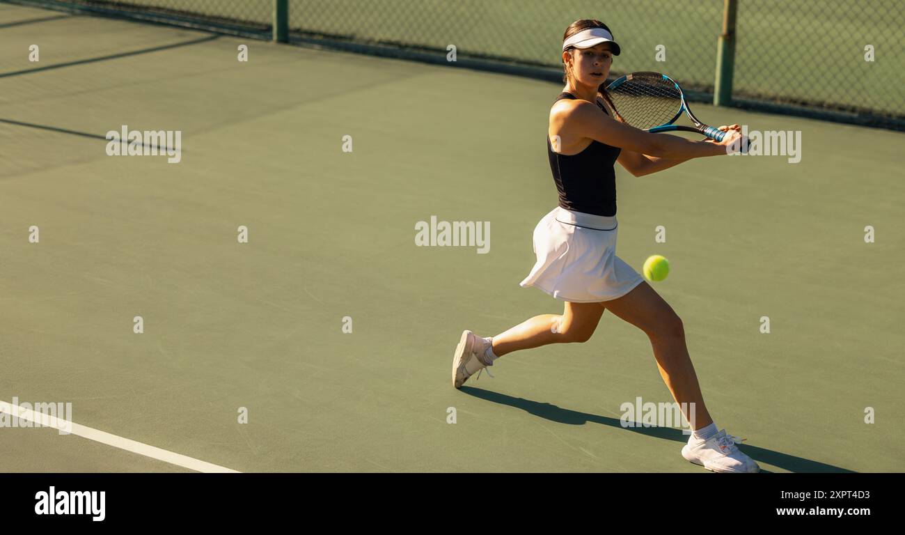 Eine Frau spielt Tennis und zeigt einen Rückhandschuss mit Schläger und Ball auf dem Platz während eines sonnigen Urlaubs. Stockfoto