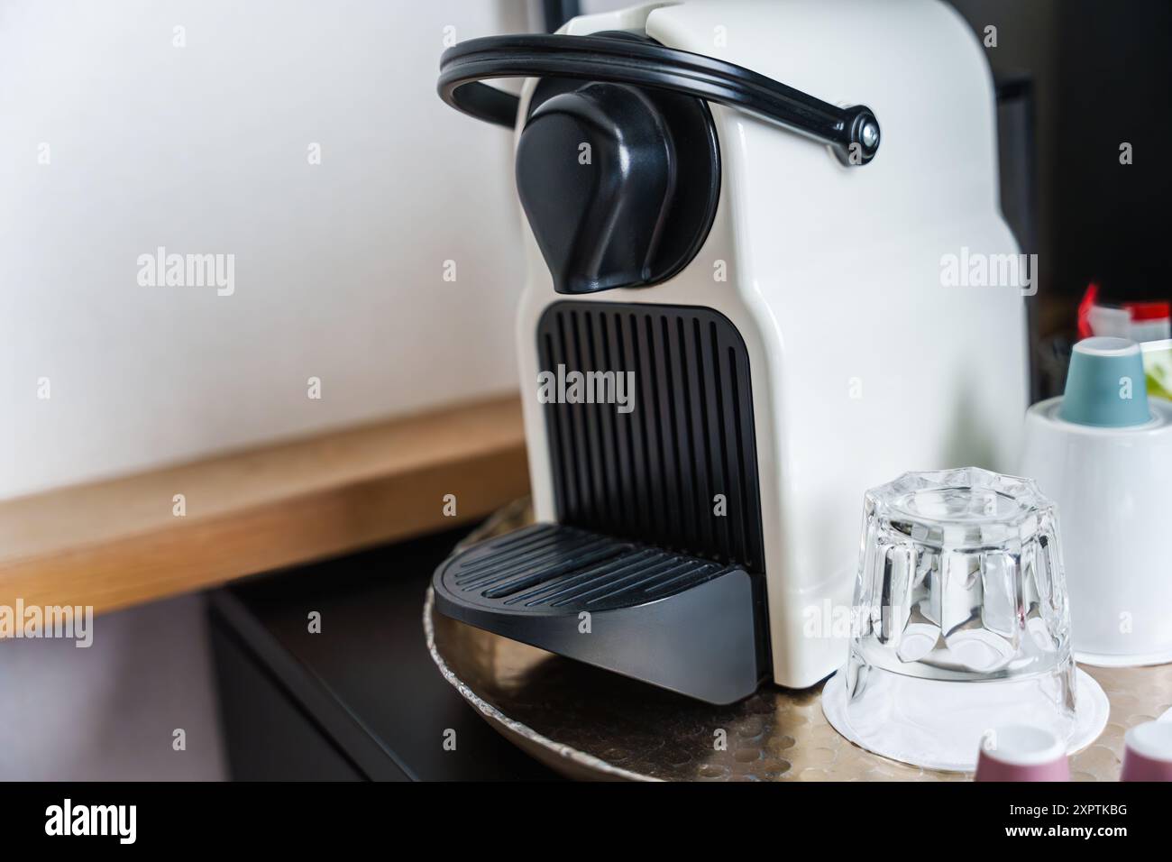 Eine moderne, kompakte Kapselkaffeemaschine mit Kaffeepads und Glas befindet sich auf einer Küchenzeile Stockfoto