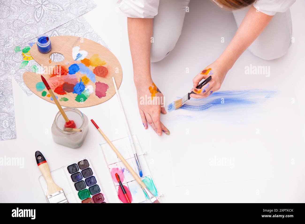 Draufsicht eines Künstlers auf Papier auf dem Boden mit verschiedenen Pinseln und farbenfroher Palette, Kreativität und künstlerischem Ausdruck Stockfoto