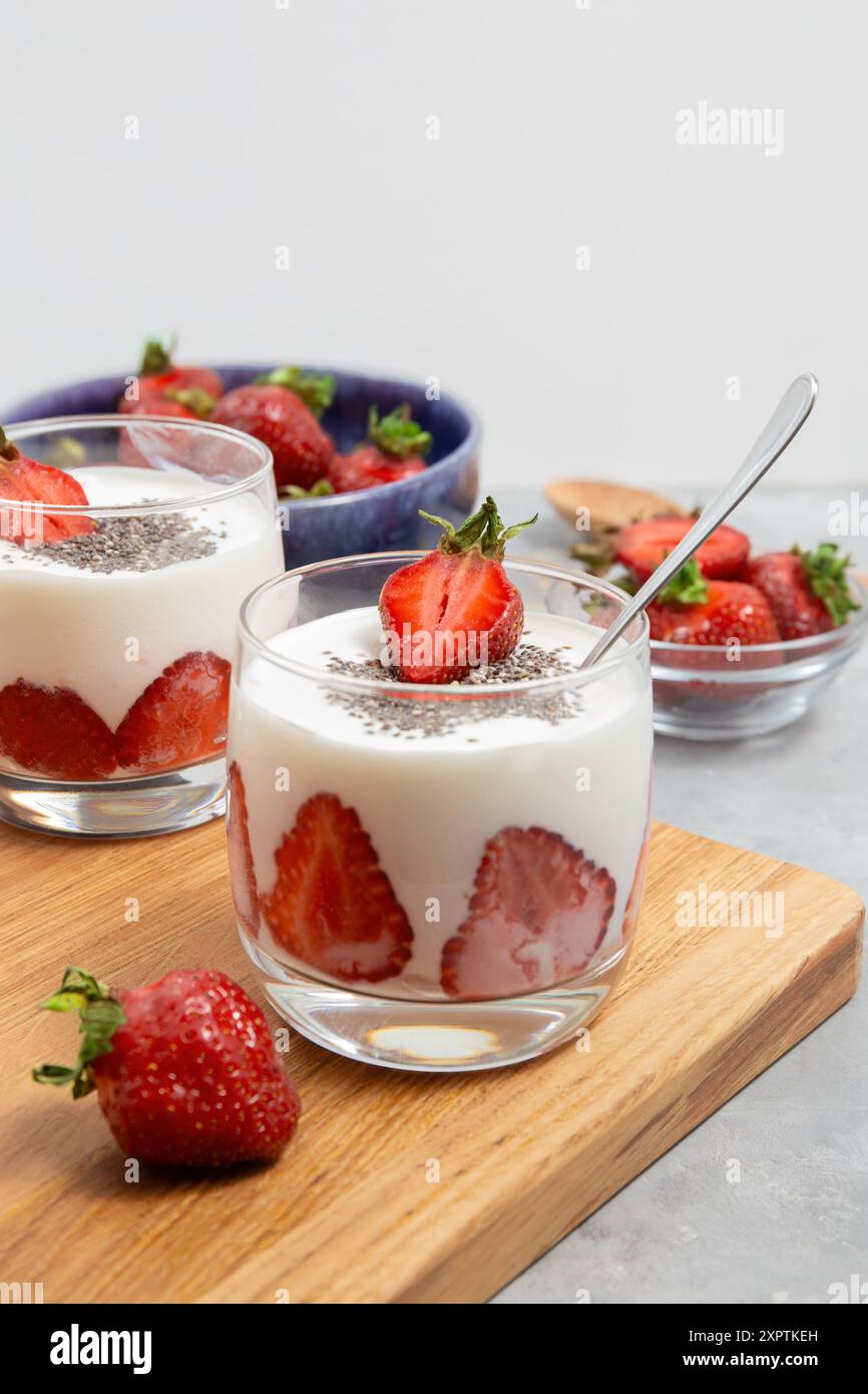 Zwei Gläser Erdbeer-Joghurt-Parfait mit Chiasamen, serviert mit frischen Erdbeeren in Schüsseln auf einem Holzbrett. Stockfoto