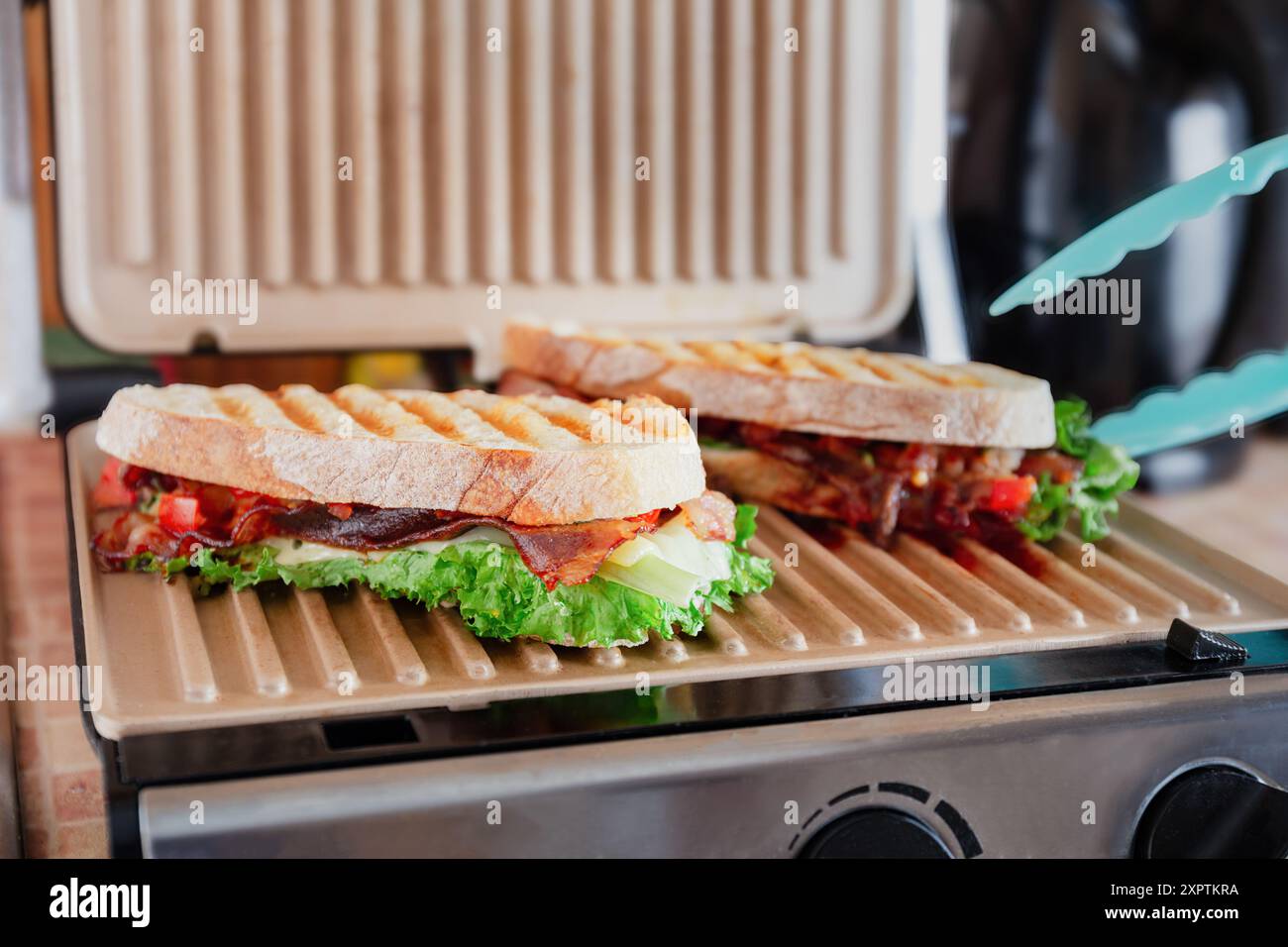 Zwei gegrillte Sandwiches mit Salat, Speck und Tomaten, die auf einer Panini-Presse in einer Küche gekocht werden Stockfoto