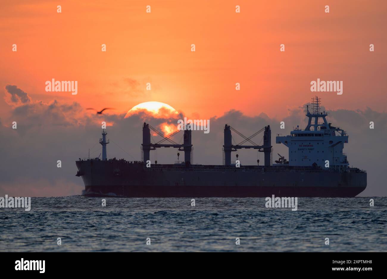 Bei der Überquerung des Sonnenaufgangs nähert sich ein Frachtschiff den Straßen in Galveston Harbor, Galveston, Texas, USA. Stockfoto