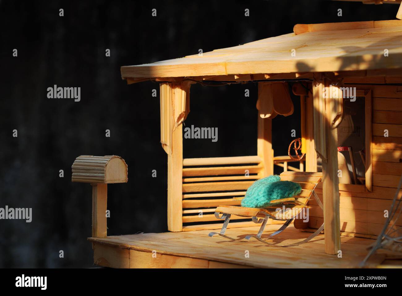 Diese Miniatur-Veranda-Szene hat einen rustikalen Charme. Es verfügt über ein Puppenhaus, helles Holz, ein Strohdach und gemütliche Liegestühle mit Türkis Stockfoto