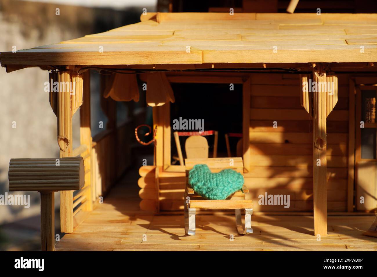 Diese Miniatur-Veranda-Szene hat einen rustikalen Charme. Es verfügt über ein Puppenhaus, helles Holz, ein Strohdach und gemütliche Liegestühle mit Türkis Stockfoto