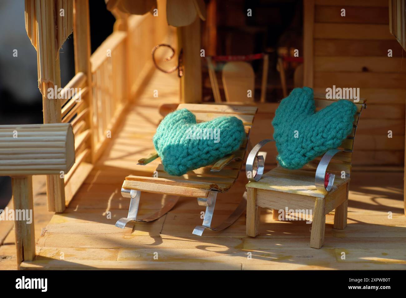 Diese Miniatur-Veranda-Szene hat einen rustikalen Charme. Es verfügt über ein Puppenhaus, helles Holz, ein Strohdach und gemütliche Liegestühle mit Türkis Stockfoto