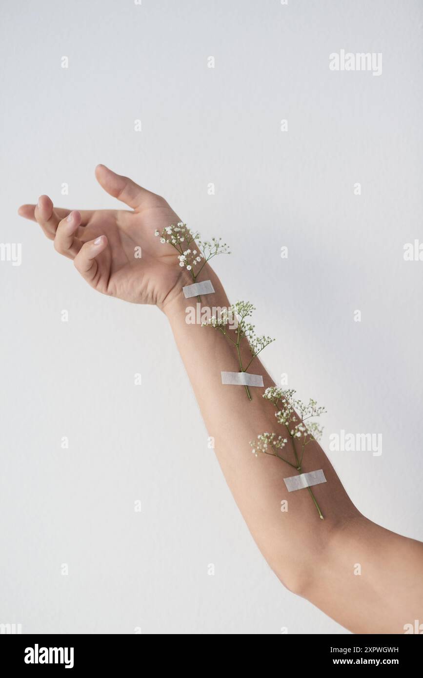 Arm, Blumen und psychische Gesundheit mit Modell im Studio für Bewusstsein, Wachstum oder natürliche Heilung. Gesundheit, Medizin und Wellness mit Person auf Grau Stockfoto