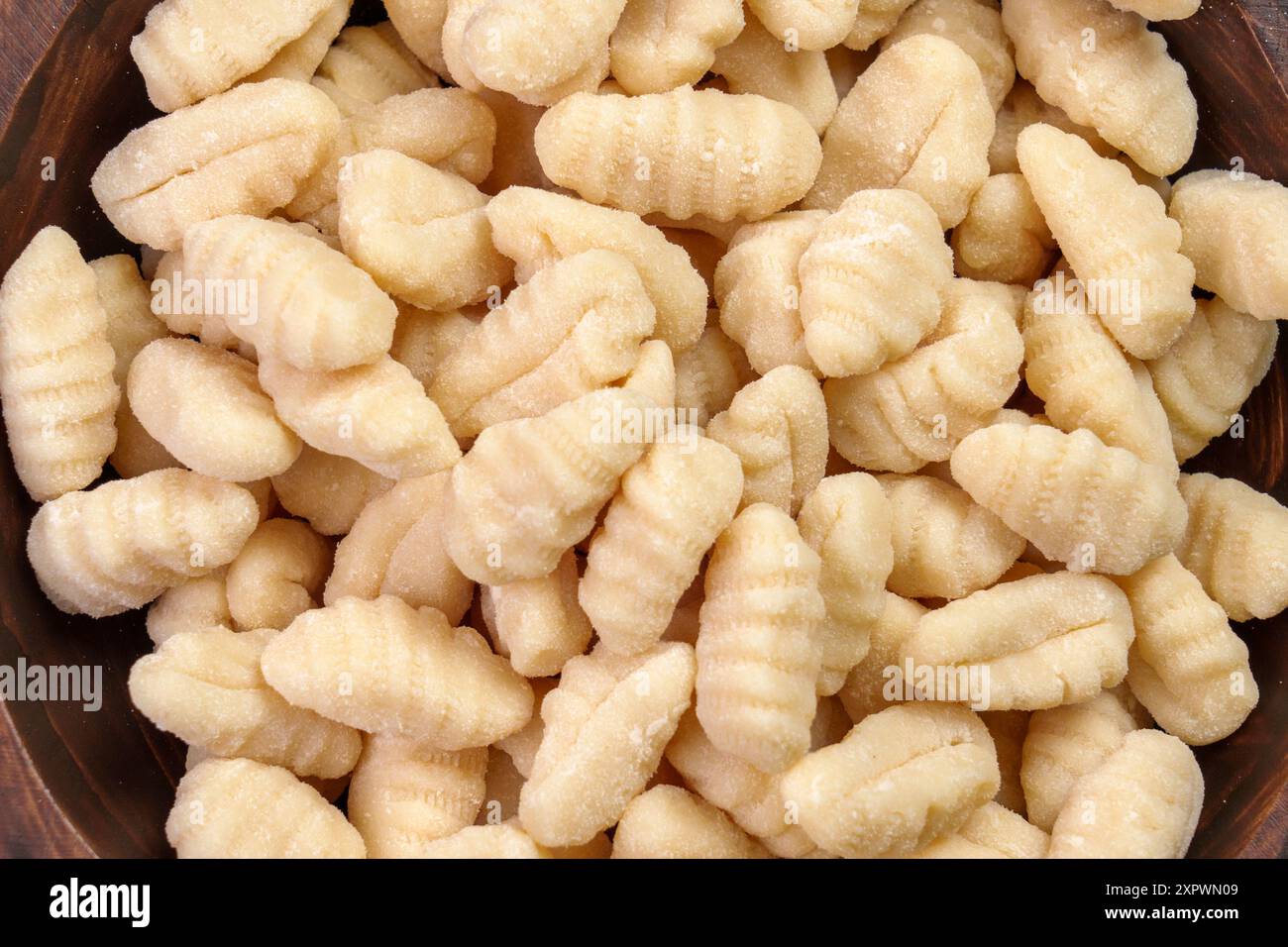 Ungekochte Kartoffelgnocchi-Knödel in Holzschüssel. Leckere rohe italienische Zutaten. Draufsicht Stockfoto
