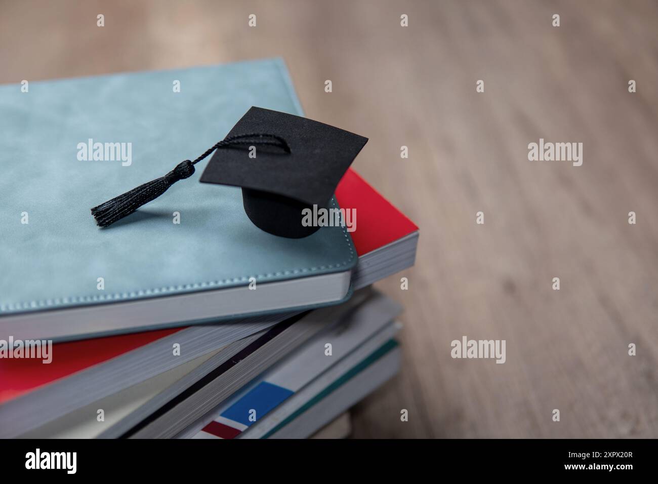 Eine schwarze Graduierungsmütze auf einem Stapel bunter Bücher. Kopierbereich für Text. Bildungs- und Wissenskonzept. Stockfoto