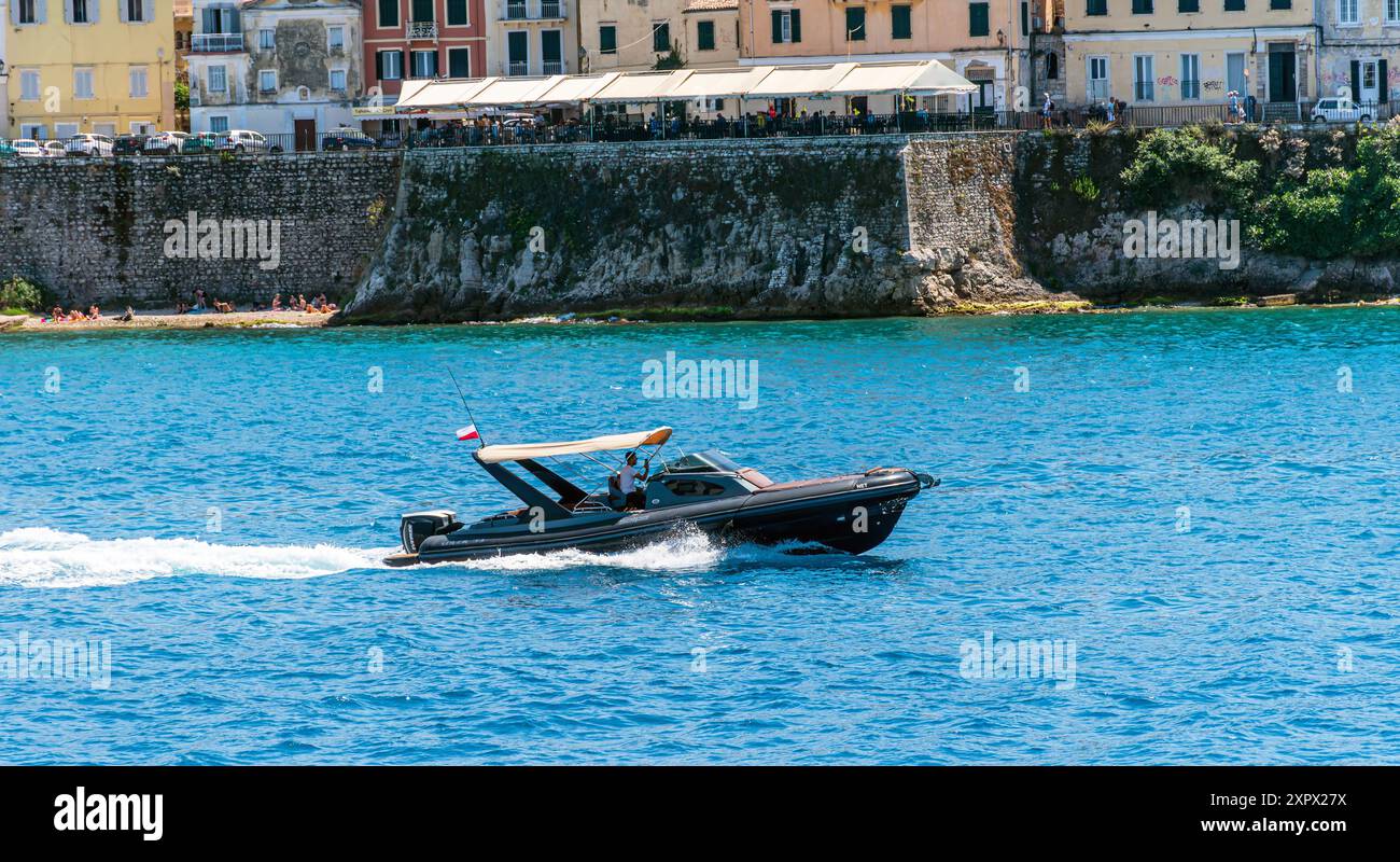 Ein Schnellboot fährt mit hoher Geschwindigkeit vor dem Hintergrund der Küste der Stadt Korfu, Griechenland. Stockfoto