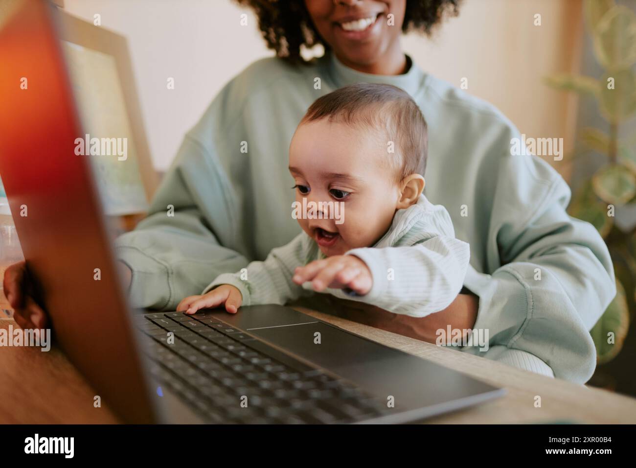 Mittlere Nahaufnahme eines neugierigen männlichen Säuglings, der den Laptop berührt, während seine Mutter ihn bewundert Stockfoto