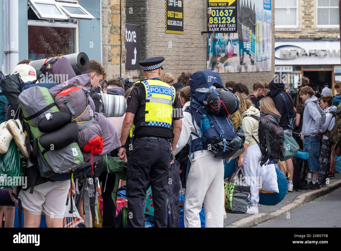 Ein britischer Verkehrspolizist hilft einigen der 1400 aufgeregten jungen Menschen, die mit einem Zug am Bahnhof Newquay ankamen, um an Bord der Busse zu gehen Stockfoto