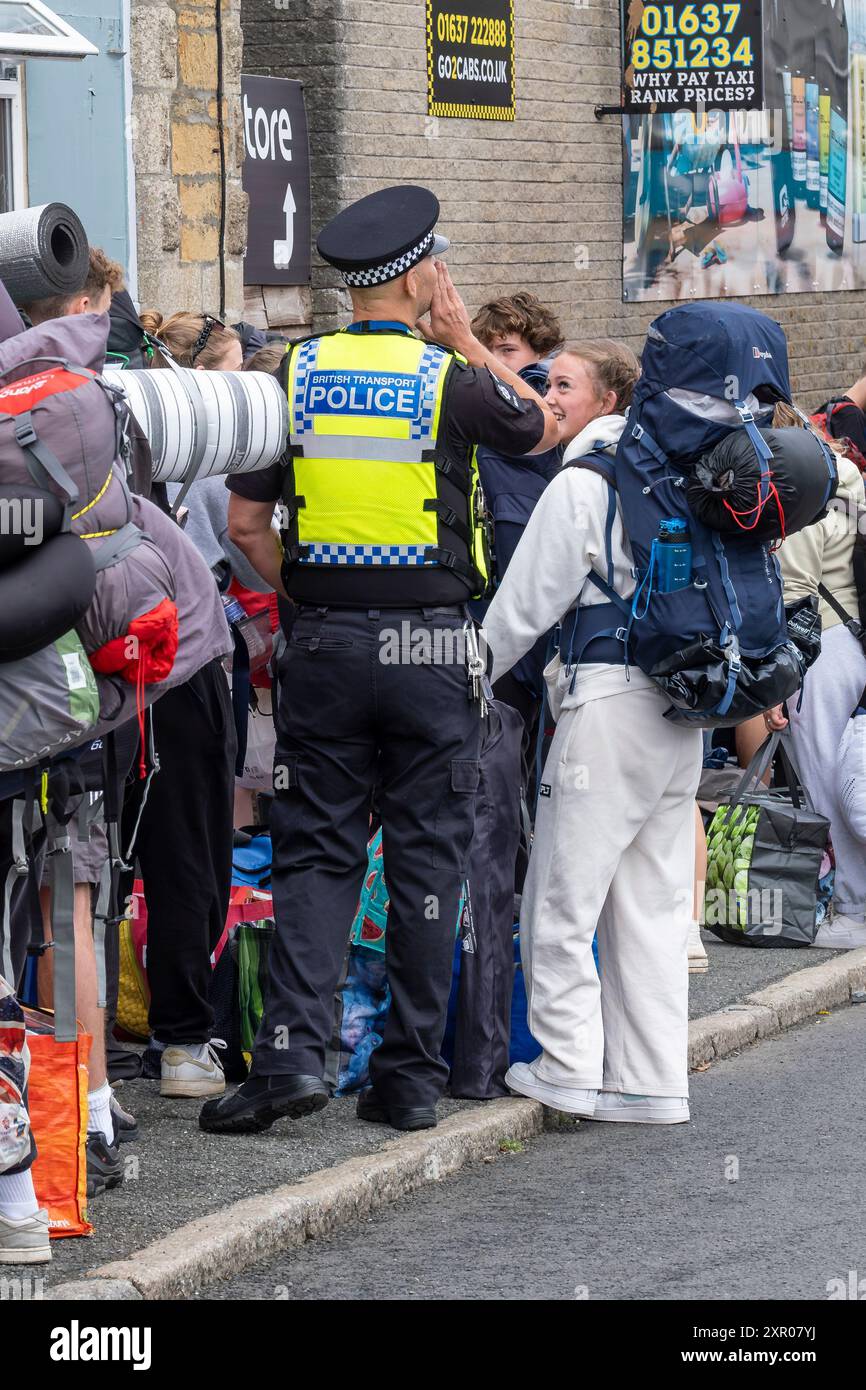 Ein britischer Verkehrspolizist hilft einigen der 1400 aufgeregten jungen Menschen, die mit einem Zug am Bahnhof Newquay ankamen, um an Bord der Busse zu gehen Stockfoto