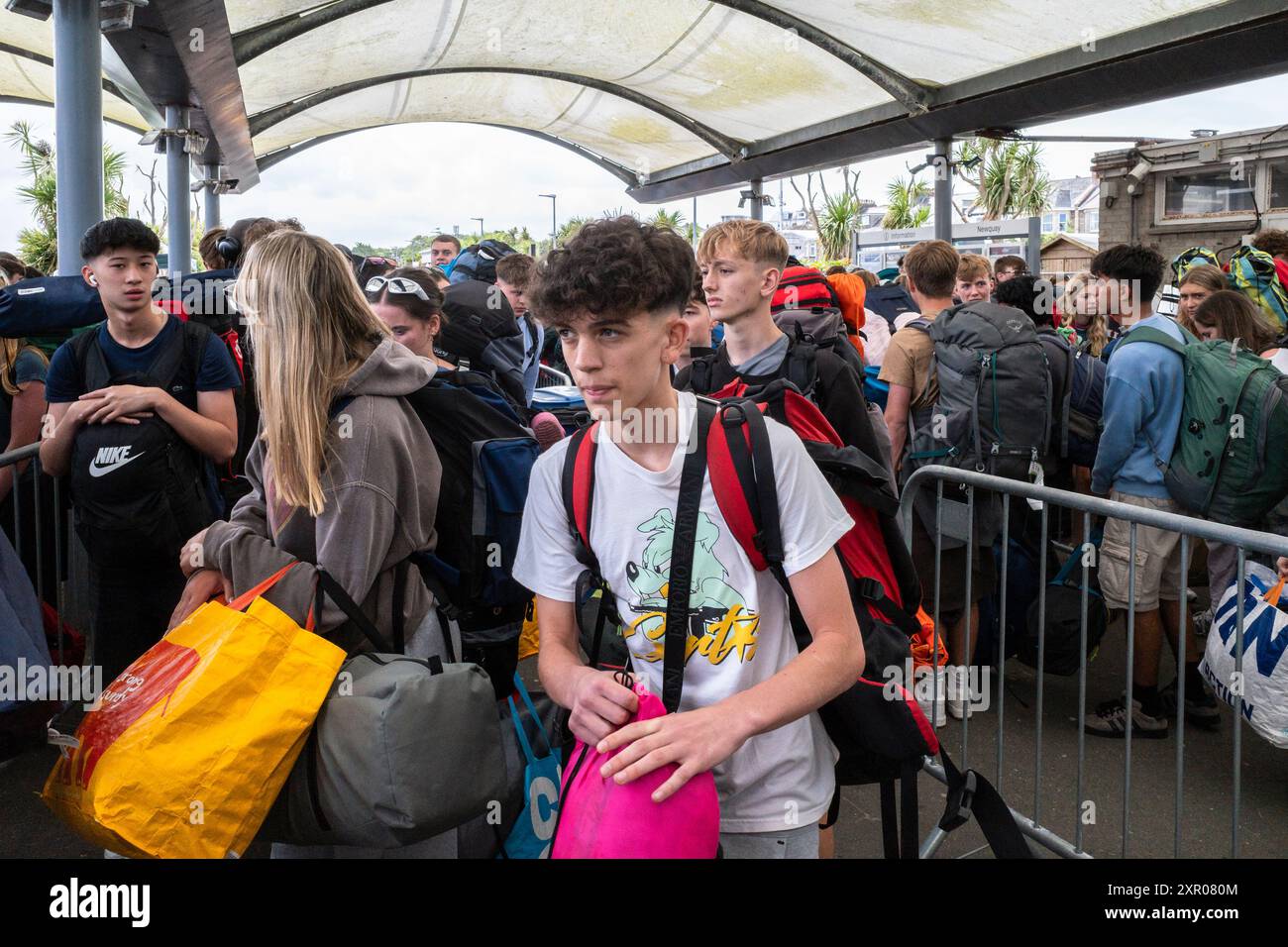 Einige der 1400 aufgeregten jungen Leute standen geduldig in der Warteschlange, nachdem sie mit einem Zug am Bahnhof Newquay zum Boardmasters Festival in Newquay angekommen waren Stockfoto