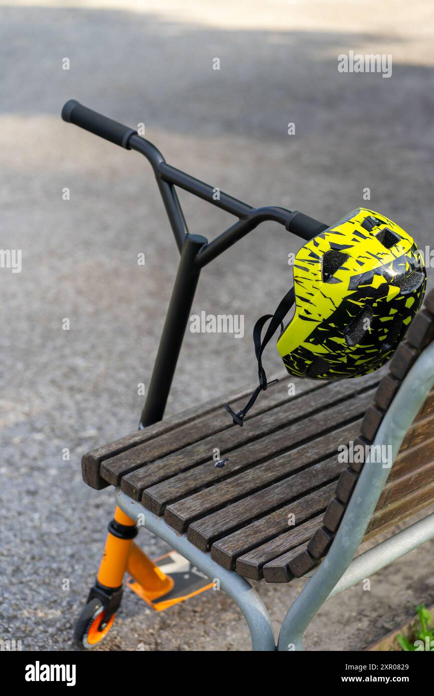 Helm und Kinder-Sportroller im Park in der Nähe der Bank. Stockfoto
