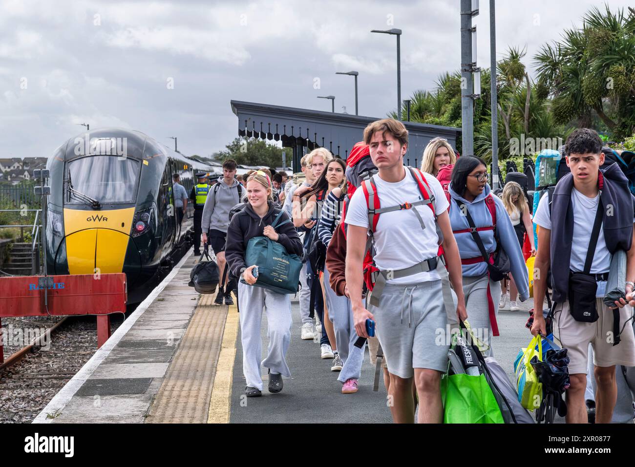 Einige der 1400 aufgeregten jungen Leute standen geduldig in der Warteschlange, nachdem sie mit einem Zug am Bahnhof Newquay zum Boardmasters Festival in Newquay angekommen waren Stockfoto