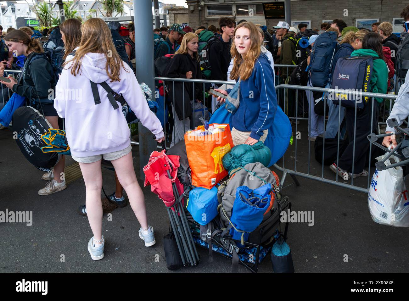 Einige der 1400 aufgeregten jungen Leute standen geduldig in der Warteschlange, nachdem sie mit einem Zug am Bahnhof Newquay zum Boardmasters Festival in Newquay angekommen waren Stockfoto