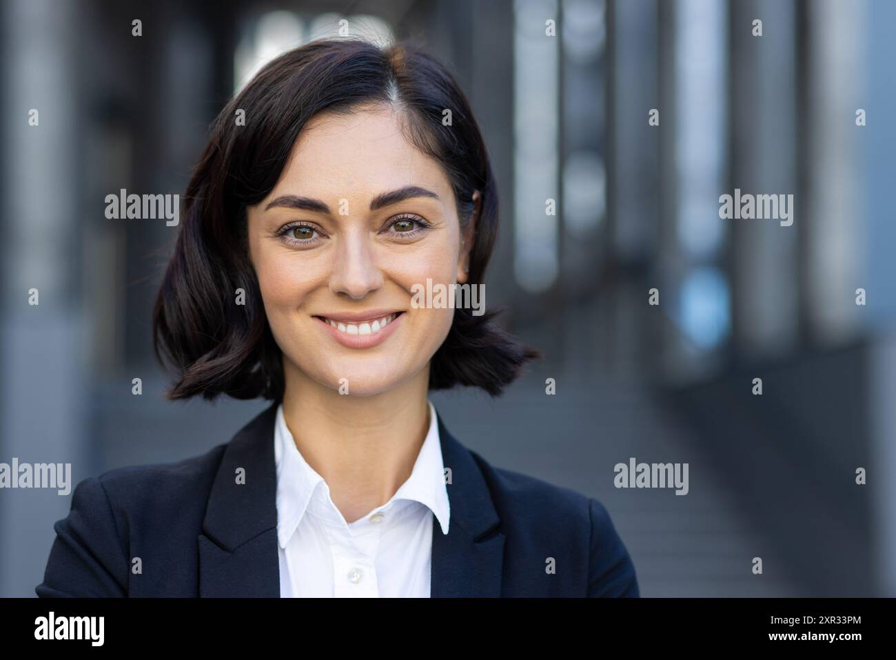 Nahaufnahme eines Porträts einer schönen jungen Frau in einem Business-Anzug, die vor einem Gebäude steht, lächelt und in die Kamera blickt. Stockfoto