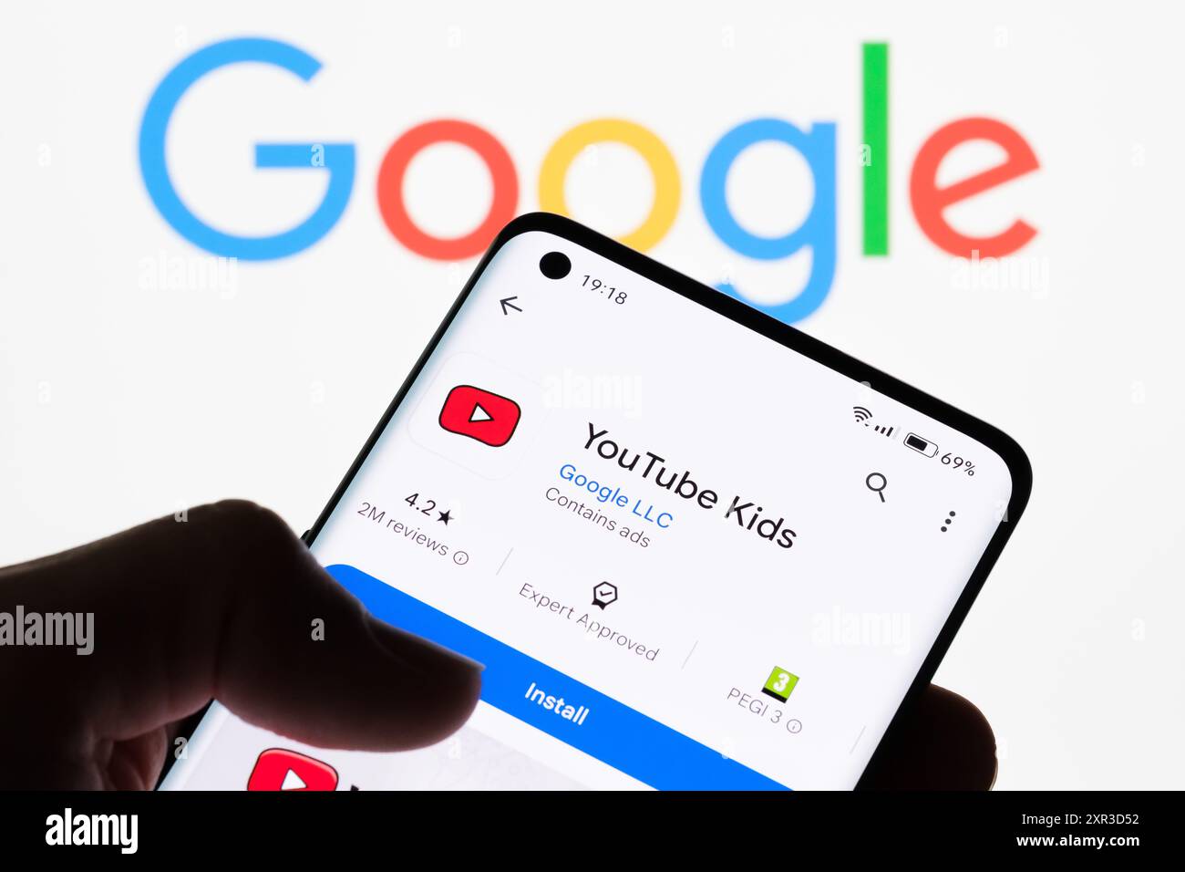 Nahaufnahme eines Smartphone-Bildschirms, auf dem die YouTube Kids App mit dem Google Logo im Hintergrund angezeigt wird, wodurch die Verbindung zwischen YouTube Kids und G hervorgehoben wird Stockfoto