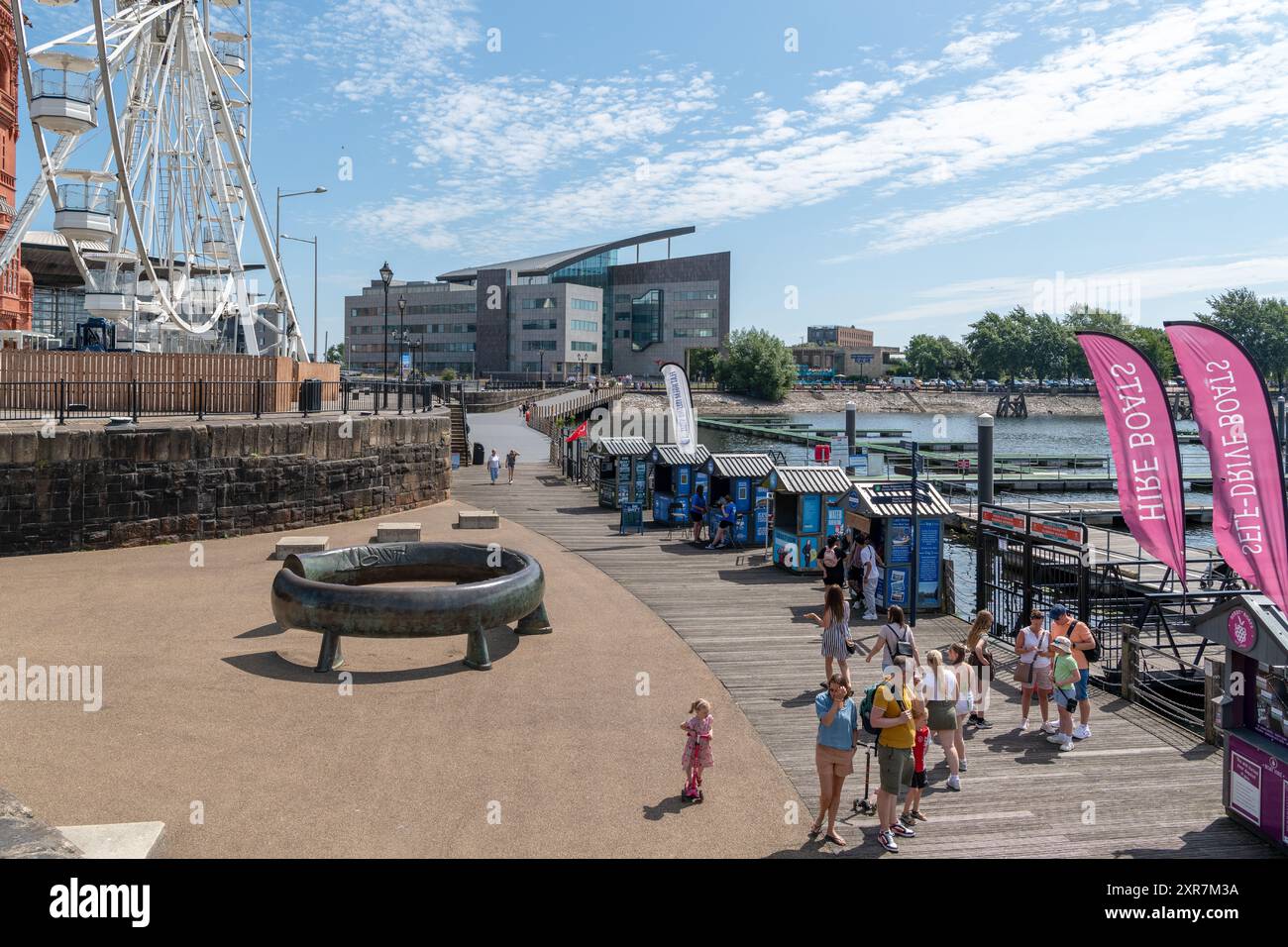 Familien genießen einen sonnigen Tag im Celtic Ring, einer großen Bronzeskulptur von Harvey Hood im Jahr 199 Ba3. Dahinter befindet sich das Riesenrad in Cardiff Bay. Stockfoto