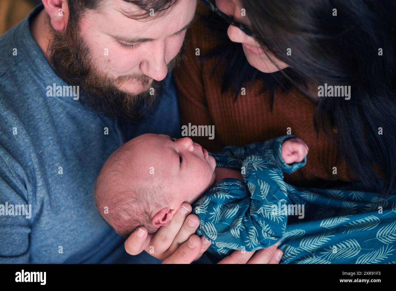 Eltern, die ihr neugeborenes Baby in einem blauen Blatt-PA liebevoll anstarren Stockfoto