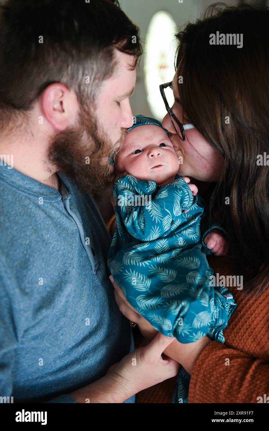 Eltern küssen ihr neugeborenes Baby in einem blauen Blattmuster Stockfoto