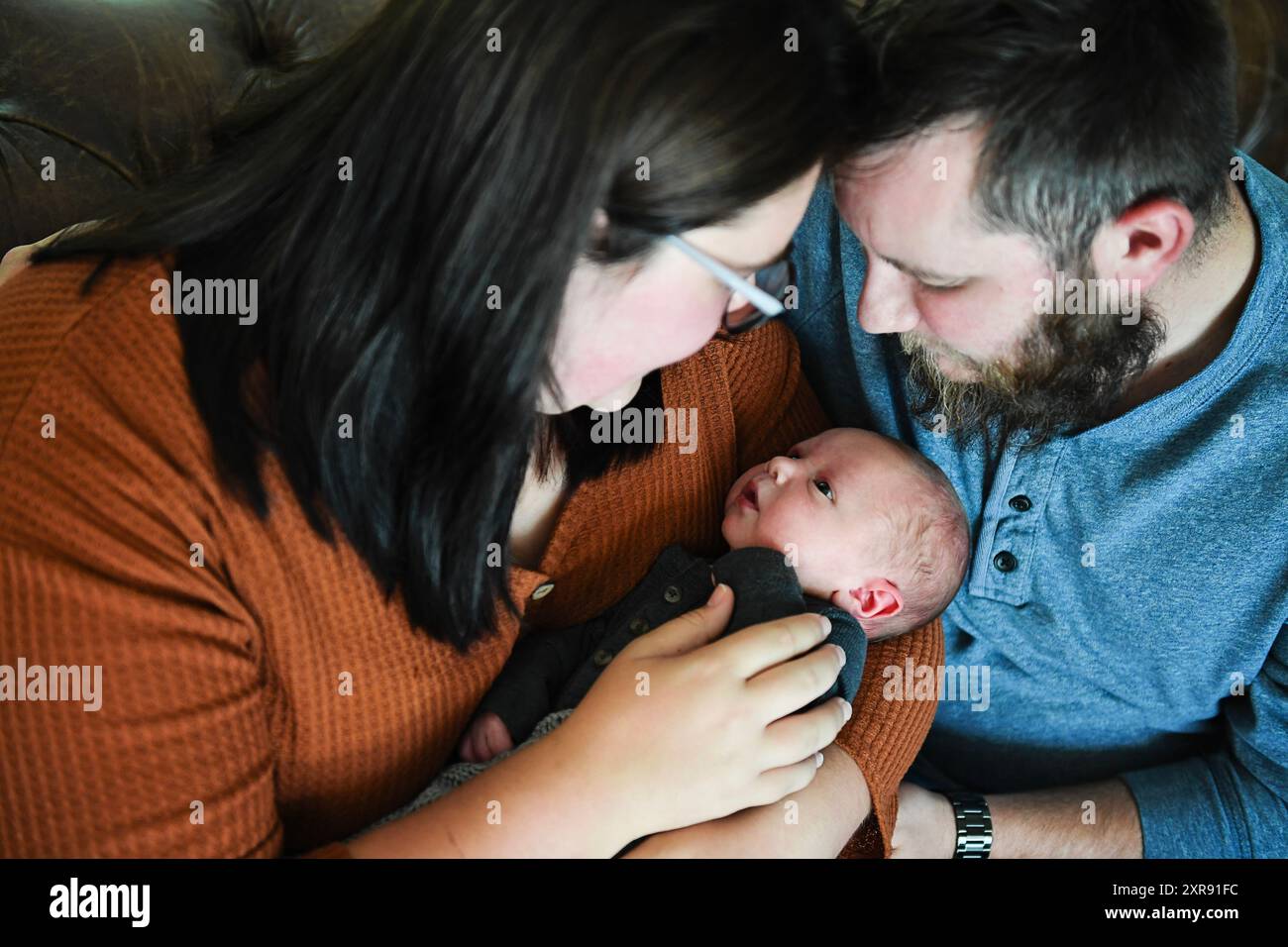 Eltern, die ihr neugeborenes Baby in grauem Outfit liebevoll ansehen. Stockfoto