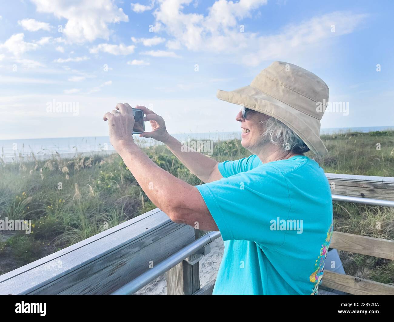 Frau mit Sonnenhut, die ein Foto an einer Strandpromenade in der Sonne macht Stockfoto