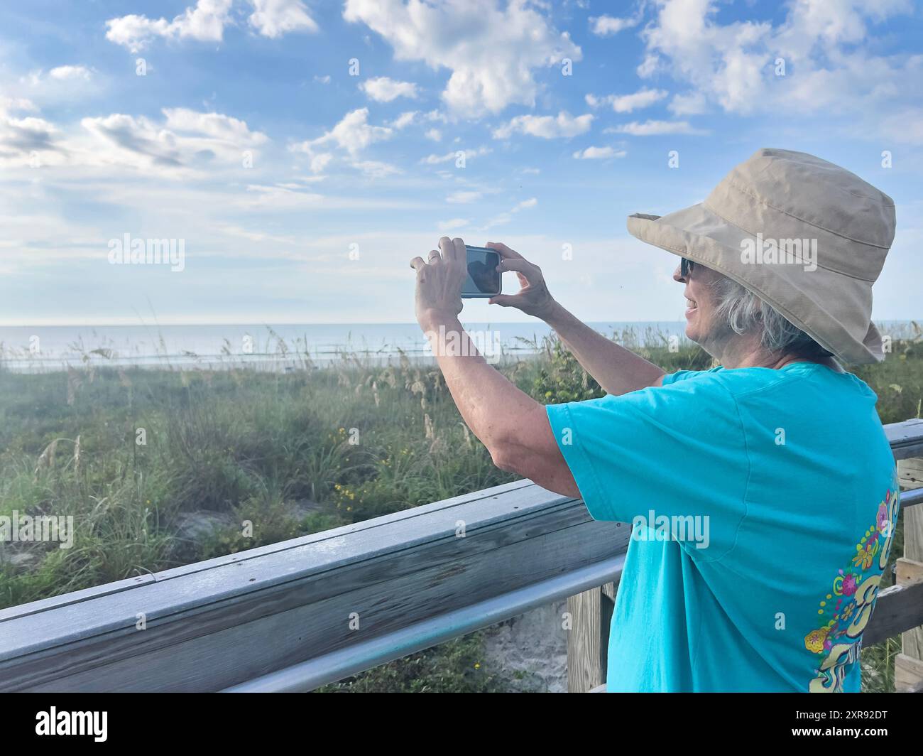 Frau in einem Sonnenhut, die ein Foto an einer malerischen Küstenpromenade macht Stockfoto