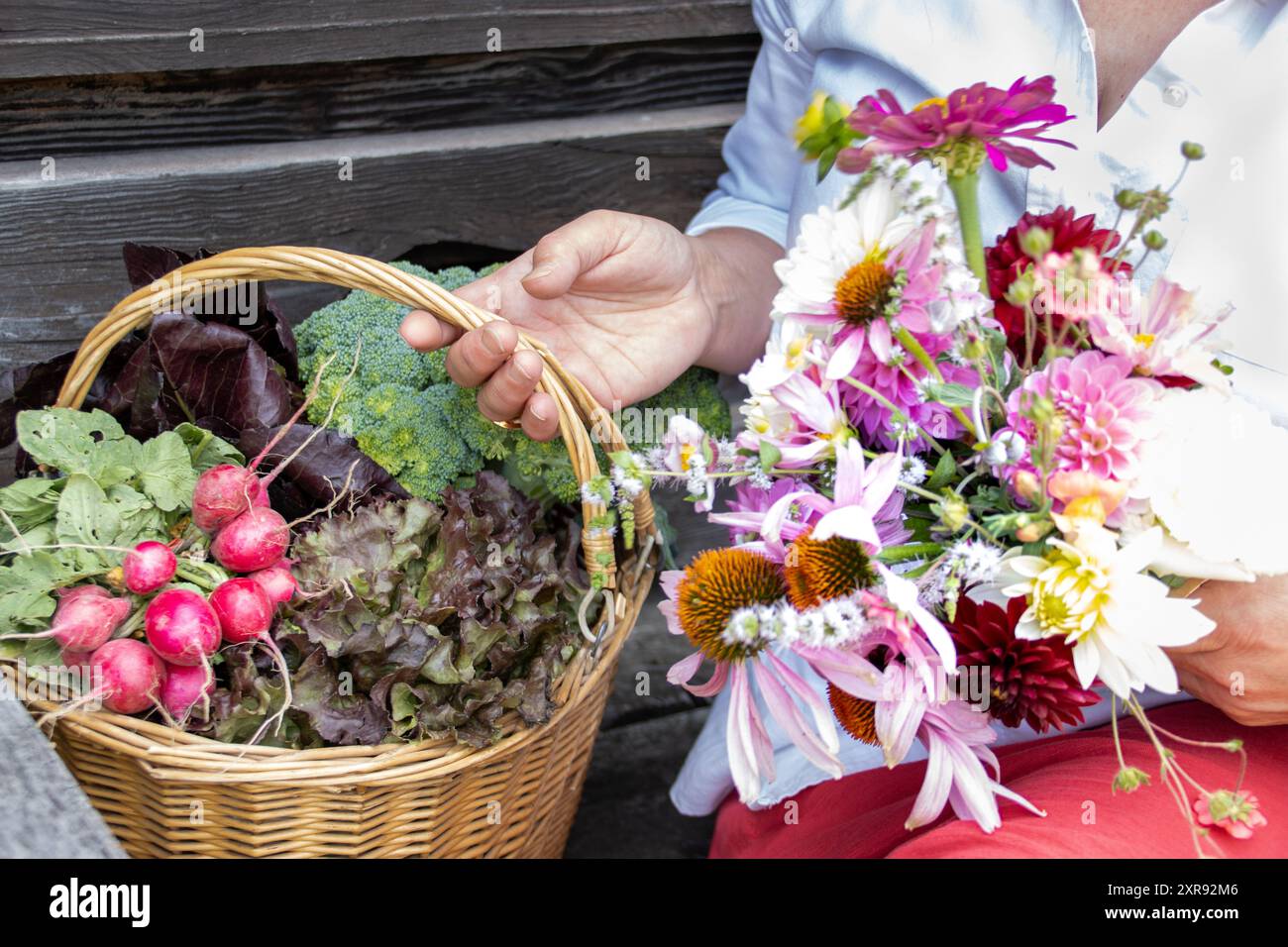 Eine Frau, die einen Korb mit frischem Gemüse und einen Blumenstrauß hält Stockfoto