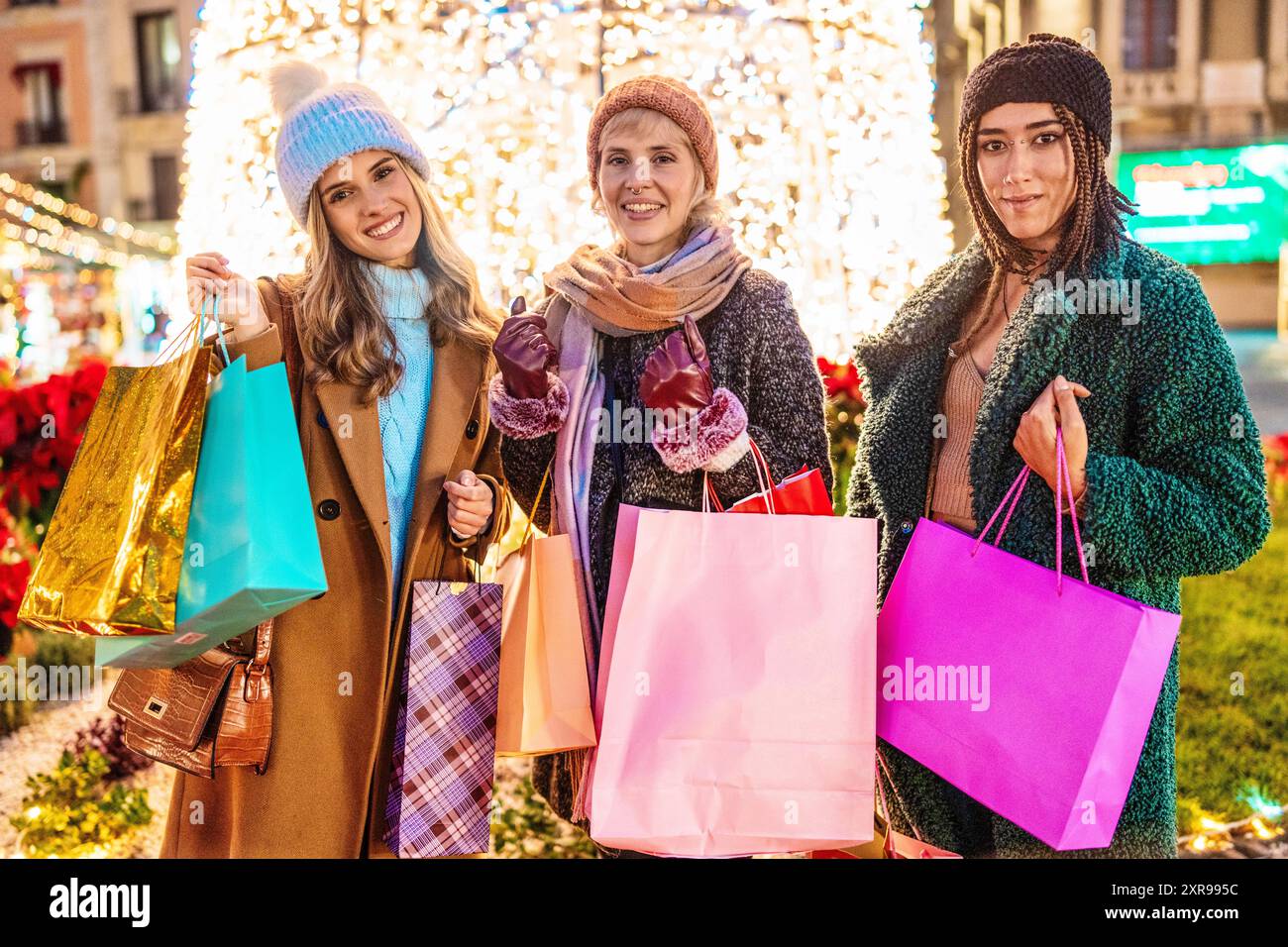 Drei stilvolle junge Frauen verschiedener Ethnien teilen sich ein fröhliches Weihnachtseinkaufserlebnis. Das Bild erfasst Vielfalt, Freundschaft und festliche Ereignisse Stockfoto