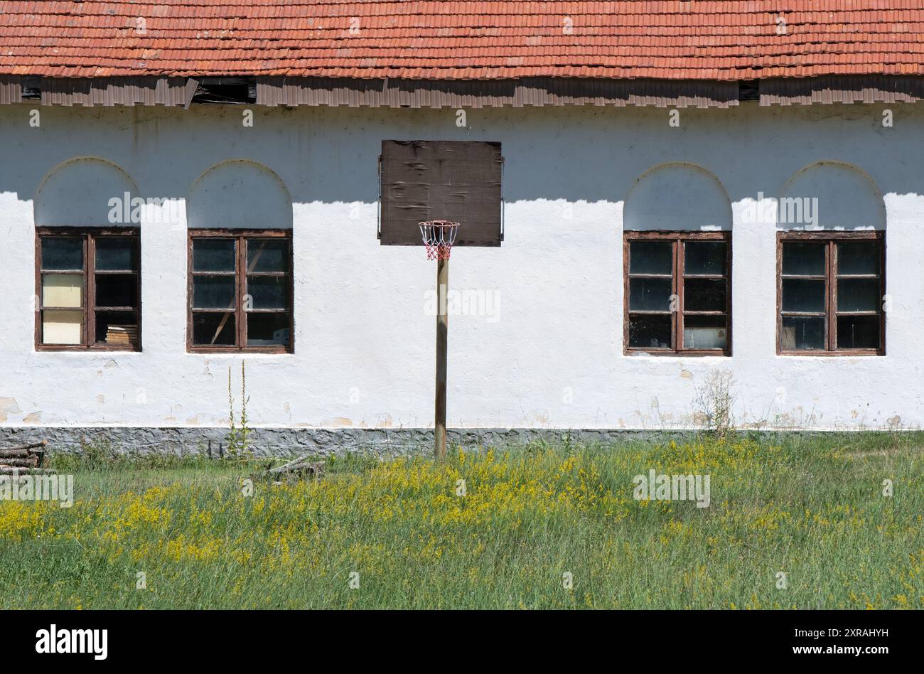 Alte verlassene Gebäudearchitektur: Schulhof mit Basketballpost und Netz, symmetrische Fensterrahmen. Stockfoto