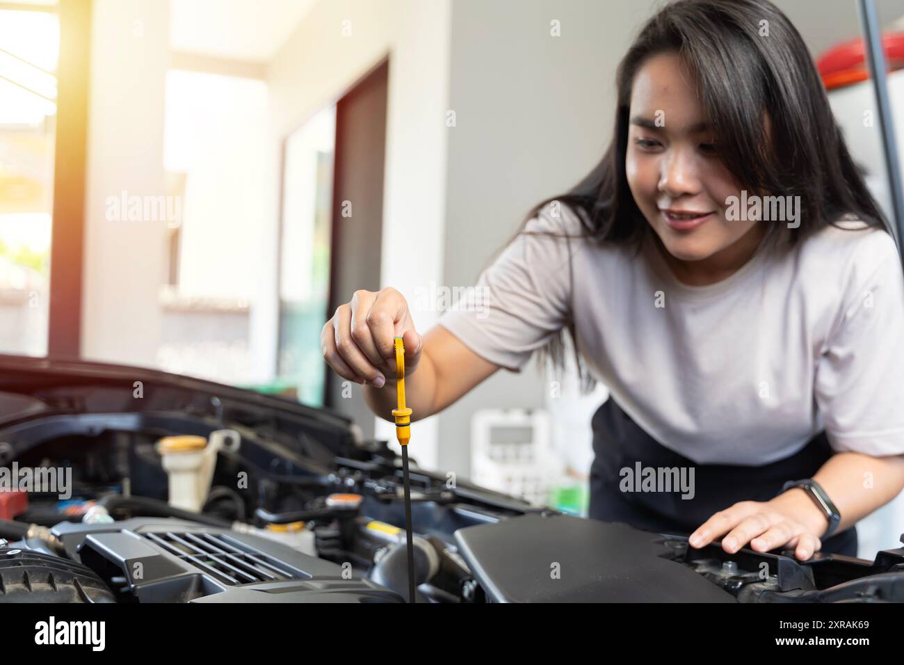 Lächelnde Frau, die Automotoröl überprüft, Automotoröl drinnen überprüft. Eine Frau kümmert sich um ein Auto in ihrem Haus, bereit zur Arbeit. Stockfoto