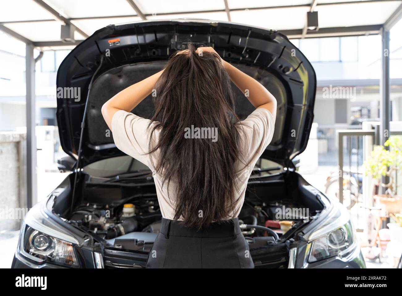 Besorgte Frau mit einem kaputten Auto, das die Motorhaube öffnet und auf den Motor blickt, während sie auf die Hilfe wartete. Eine besorgte Frau öffnet die Motorhaube ihres Autos Stockfoto