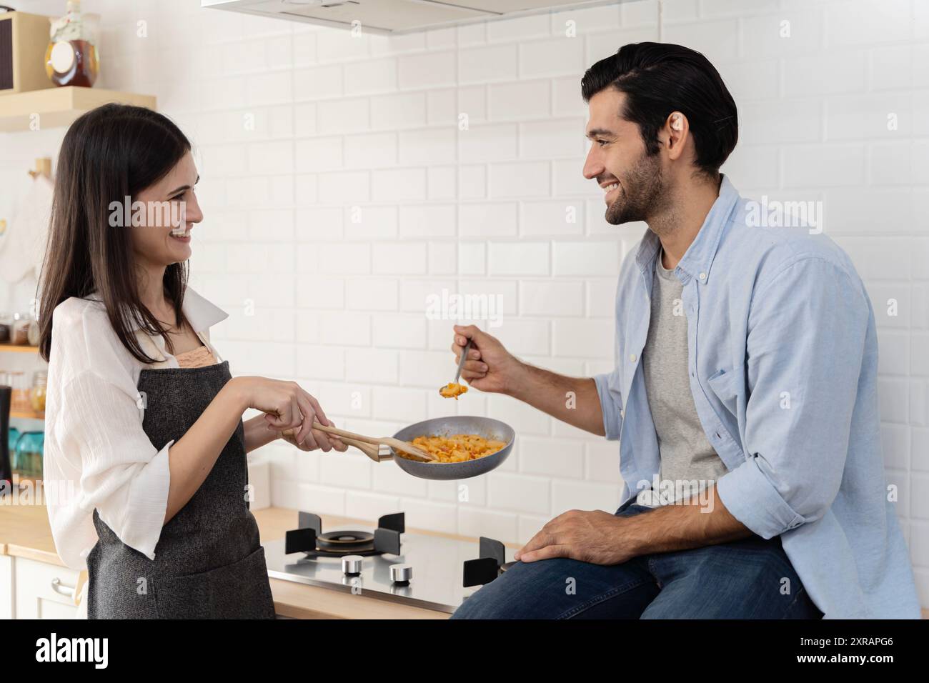 Glückliches Paar, das in der Küche sitzt und Spaghetti isst. Lachen mit glücklicher Frau und Haschband essen Pasta in heller Küche romantisches Abendessen im h Stockfoto