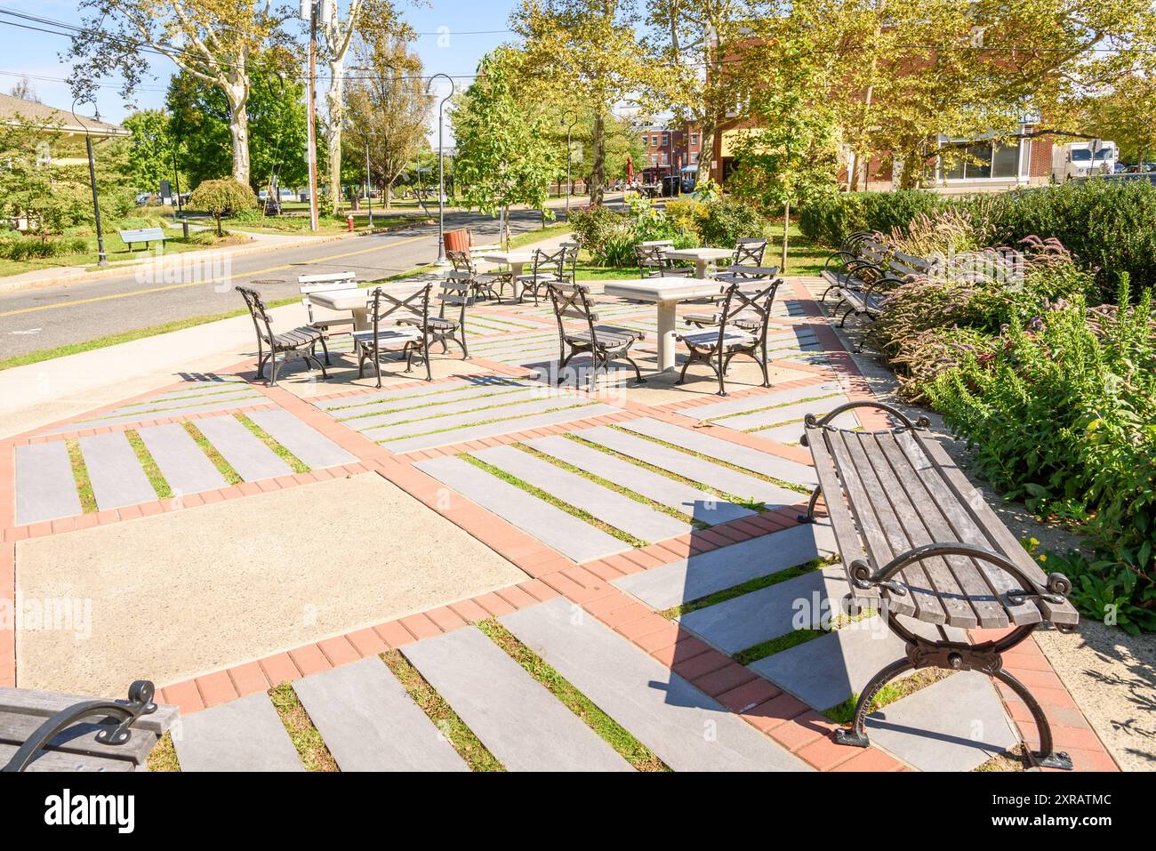 Feste Betonschachtische und Holzbänke in einem verlassenen kleinen Park entlang einer Straße in einer historischen Innenstadt an einem sonnigen Herbsttag Stockfoto