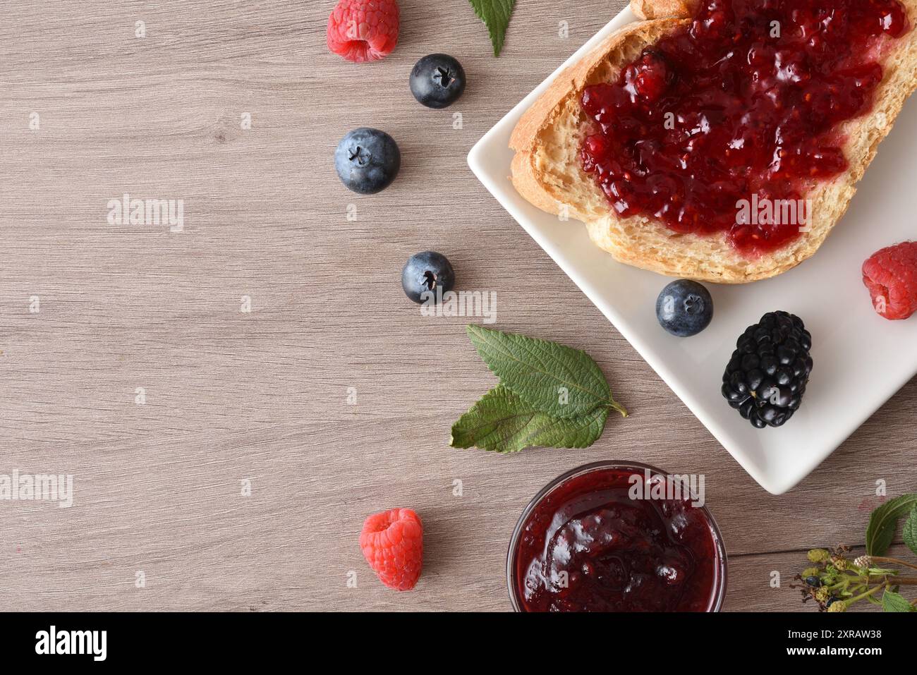 Tisch mit wilder Beerenmarmelade in einer Schüssel und auf einer Brotscheibe auf einem Holztisch verteilen. Draufsicht. Stockfoto