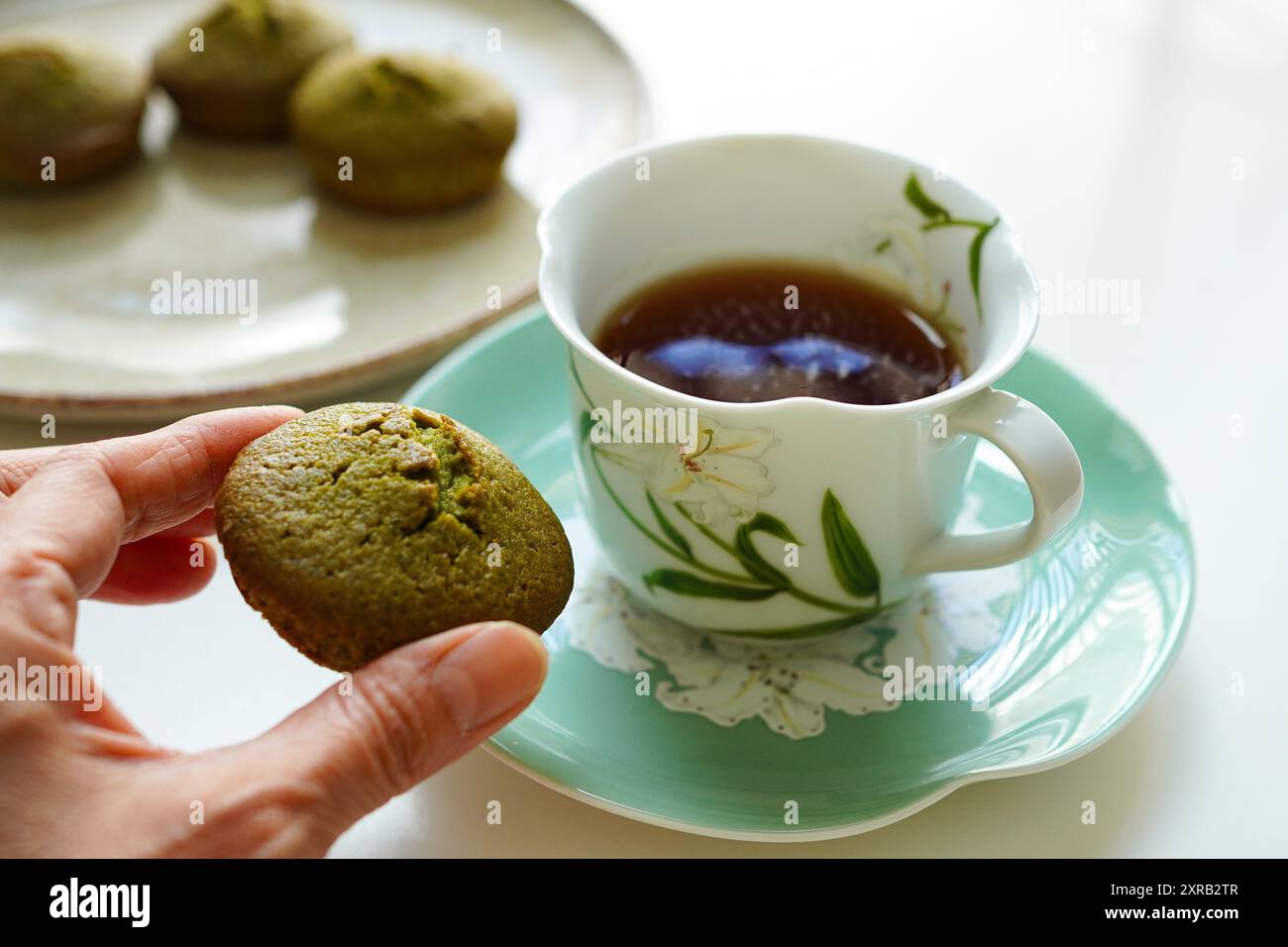 Frau genießt Teezeit mit Matcha-Grüntee-Kuchen und schwarzem Tee Stockfoto