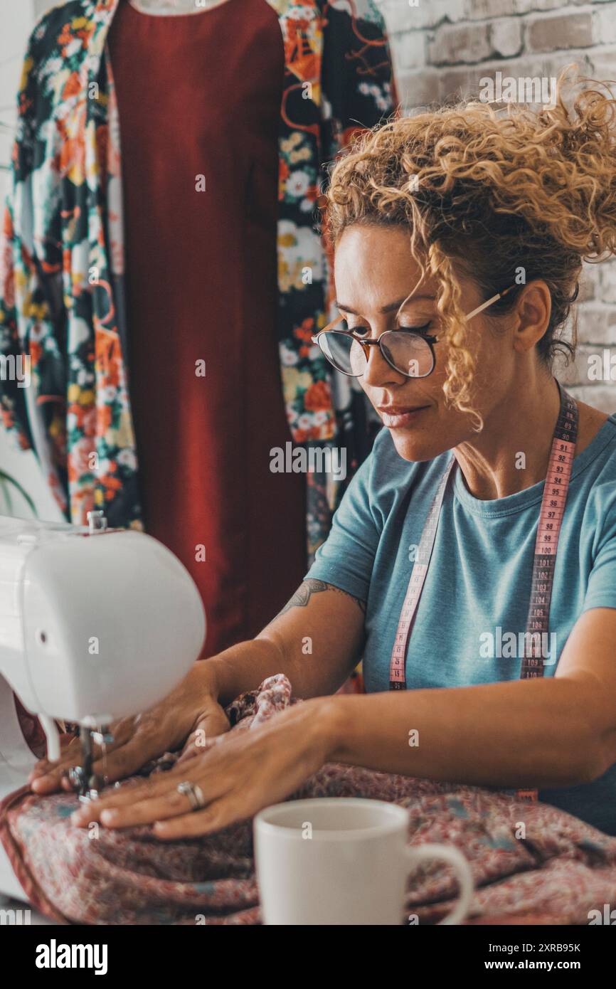 Eine Arbeiterin zu Hause oder in der Werkstatt, die Nähmaschine als Näherin benutzt und mit ihr arbeitet. Glückliche Arbeiterinnen mit alternativen Geschäften zu Hause Stockfoto