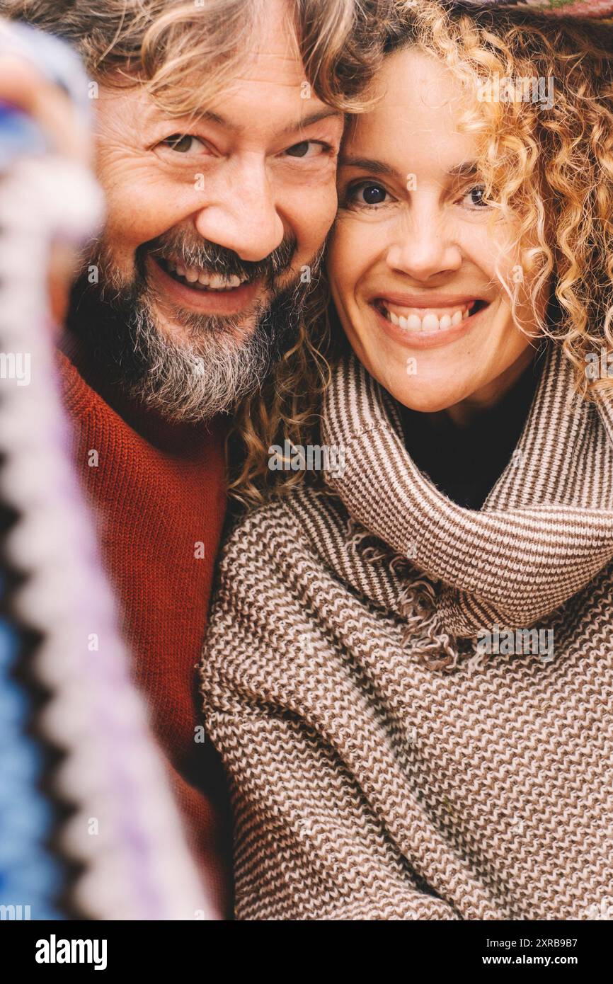 Porträt eines jungen, reifen Paares, das lächelt und gemeinsam unter einem bunten Strickmantel aus Wolle die Freizeit genießt. Liebe und Freundschaft zwischen Mann und Frau. Menschen, die Spaß haben und lachen. Urlaub Stockfoto