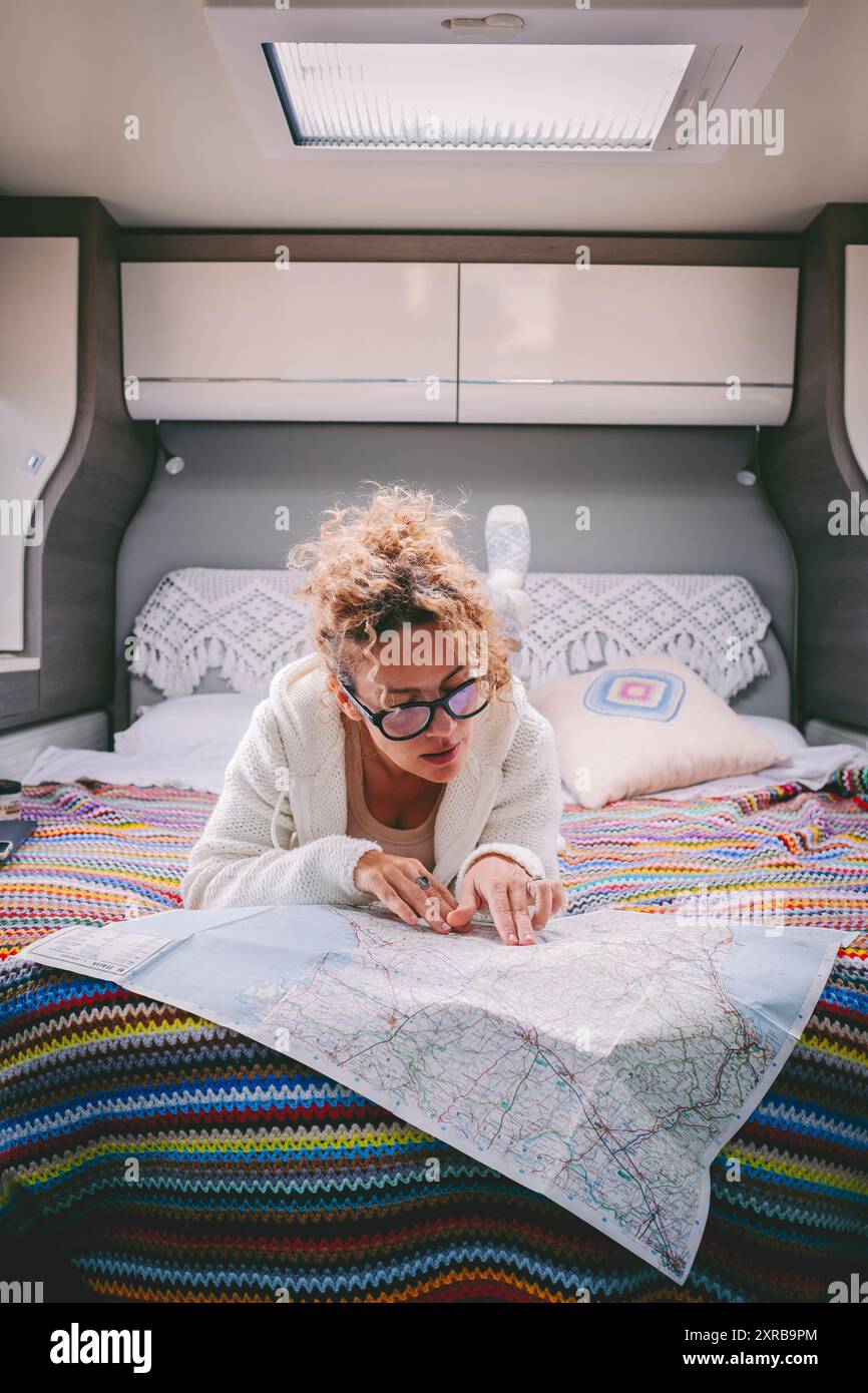 Eine Frau, die das nächste Reiseziel plant, liegt in einem mpodernen Wohnmobil im Bett. Menschen und Vanlife Lifestyle Reisende. Weiblich aussehende Papierkarte für Roadmap Indoor Freizeit Stockfoto
