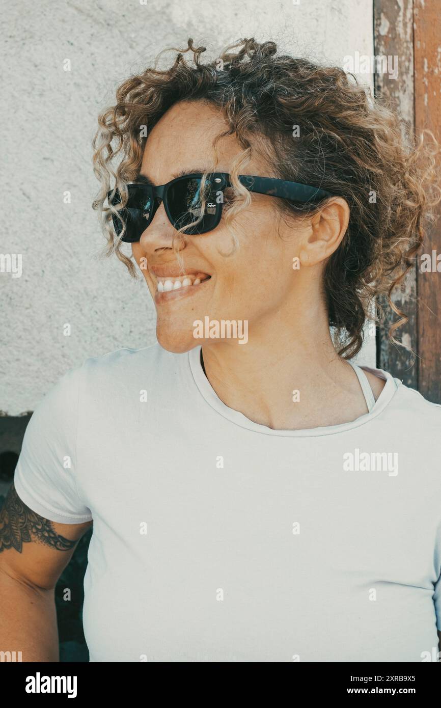 Glückliches Porträt der Frau in Outdoor-Freizeitaktivitäten im Garten zu Hause. Junge Erwachsene Frauen lächeln und tragen allein eine schwarze Sonnenbrille. Fröhliche Dame, die Zeit vor ihrem Haus genießt Stockfoto