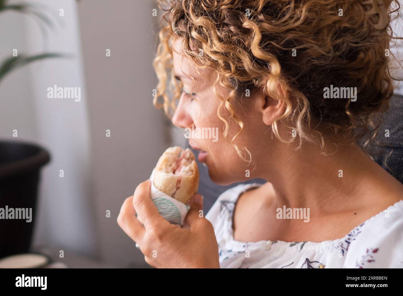 Eine ungesunde Frau, die Sandwich isst und zu Hause auf dem Laptop arbeitet, sitzt auf dem Sofa. Schlechte Ernährungsgewohnheiten. Nehmen zu essen Junk Food. Fastfood-Mittagessen während der Arbeitszeit im Innenbereich Stockfoto