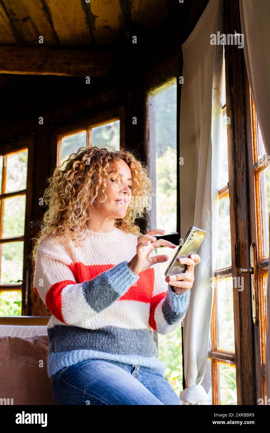 Eine erwachsene Frau, die allein bei der Online-Freizeitaktivität im Innenbereich zu Hause per Telefon liest und Nachrichten sendet Stockfoto