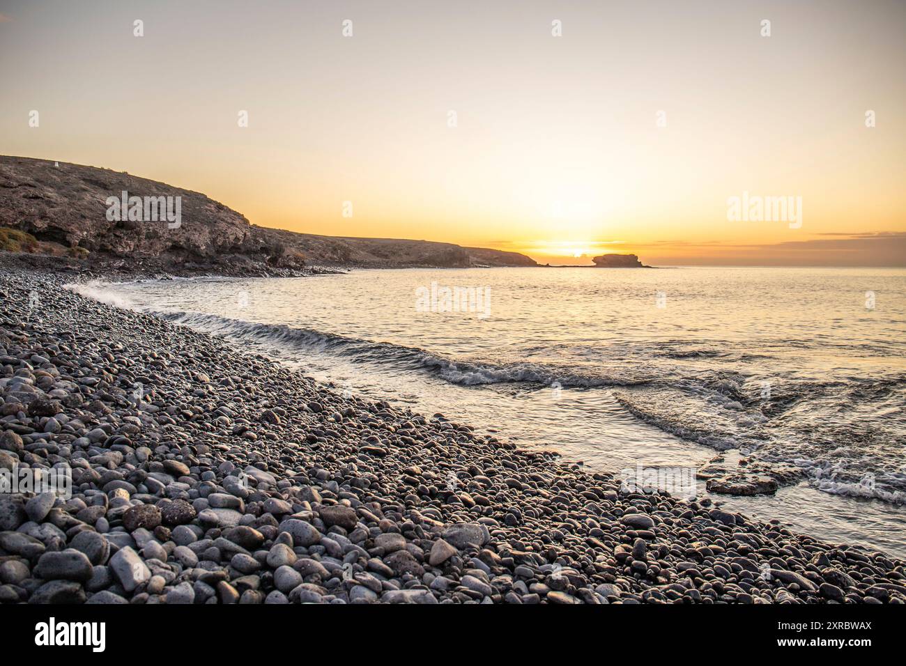 Blick auf den Sonnenaufgang über dem Atlantik. Blick über einen Steinstrand auf einer Vulkaninsel. Kalte Lavasteine am Meer am Strand von Playa Laja del Corral, Fuerteventura, Kanarischen Inseln, Spanien Stockfoto